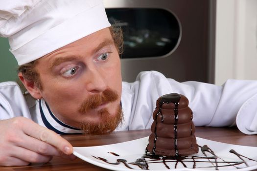 Funny young chef strange looking at piece of cake with chocolate sauce