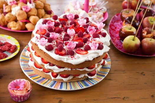 Table filled with a variety of birthday snacks like a layered cake, cupcakes and taffy apples