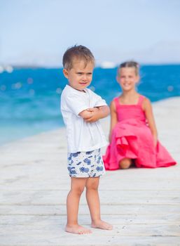 Cute toddler boy with his sister walking on jetty with turquoise sea