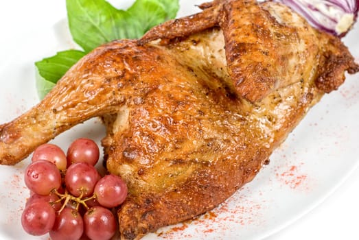 Half roasted chicken closeup with grape and greens on a white