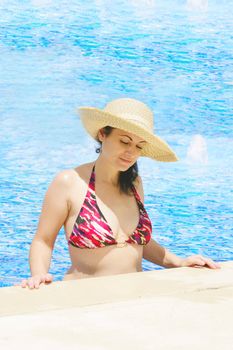 The beautiful woman in a hat in pool
