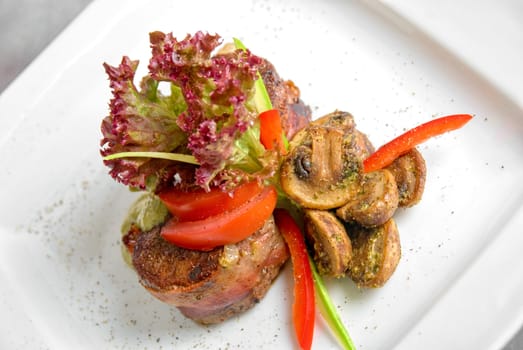 Tasty beef steak grilled in a cast-iron ribbed fry pan with bacon decorated with vegetables and roasted mushrooms