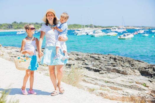 Young beautiful family of three walking along tropical beach