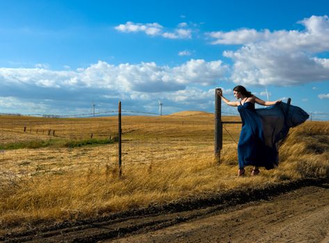 Girl with a designer silk dress near the wind turbines. 