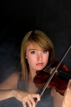 Girl playing violin during a performance with the stage covered in fog. 