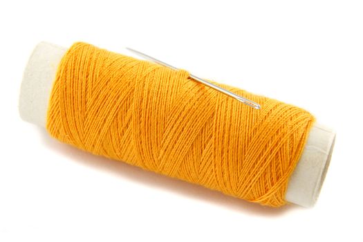 Orange thread bobbin with needle on white background