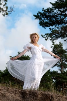 Woman stands near precipice. Wind blows the white dress.