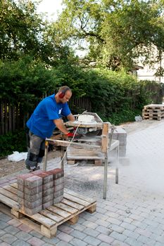 worker with circular saw sawing bricks for new street