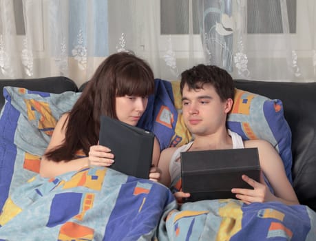 Young lively couple using tablet PC in their bed