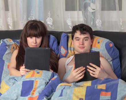 Young lively couple using tablet PC in their bed