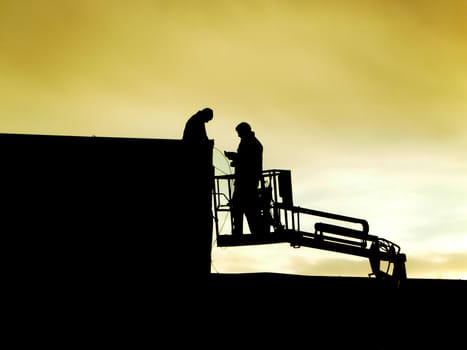 Silhouettes of men working at night.
They are working on a roof, one worker is in a lift
