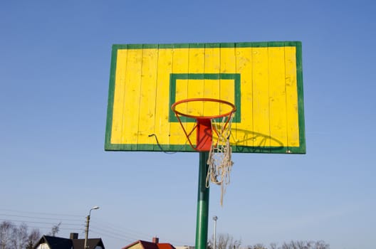 Basketball basket with tattered bow mesh on background of blue sky. Colorful active leisure game object.