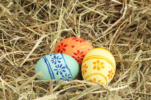 Three colored Easter eggs on hay at sunny day