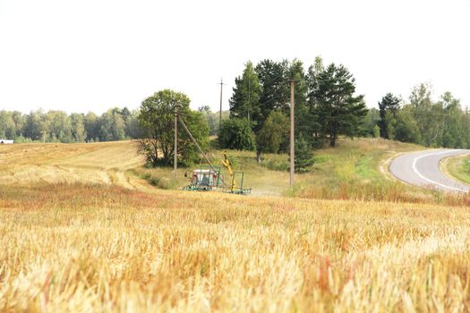 Tractor with hay at yellow wheat field in summer day 