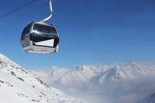 Chairlift in mountains and panoramic view on winter alps under blue sky