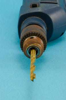 old electric drill with golden bit and rosette plug closeup on blue background.