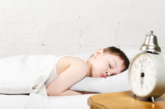 Small toddler boy (4 years old) is sleeping in bed. Old clock show 6 o'clock. Brick wall