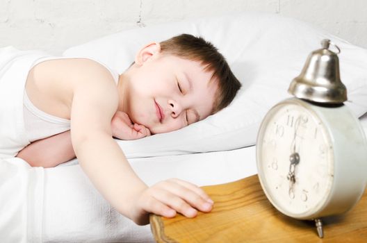 Small toddler boy (4 years old) is sleeping in bed. Old clock show 6 o'clock. Brick wall