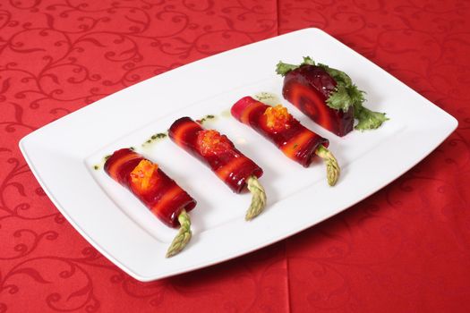 Vegetable rolls with asparagus and red beet on a white plate