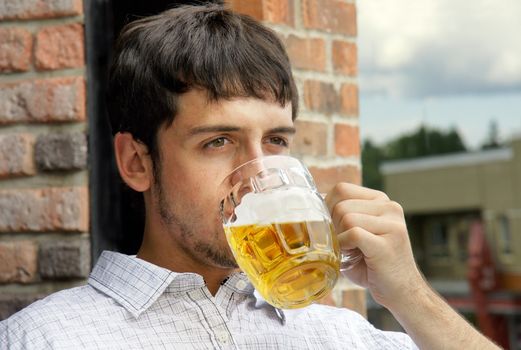 Portrait of a sad young man drinking beer out of glass bok on pub's outdoor terrace.