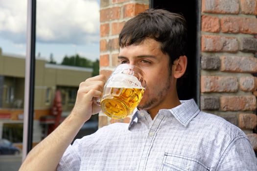Young man drinking beer in glass bock, could be student or alcoholic.