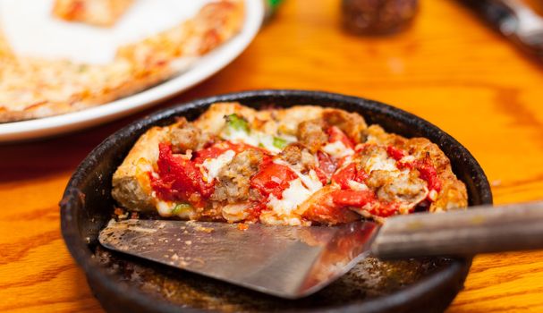 Wooden table with deep-dish personal pizza with serving knive and other meals