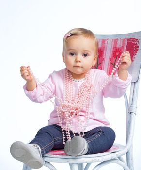Portrait of an adorable baby girl wearing a pink with pearl necklace sitting on a c