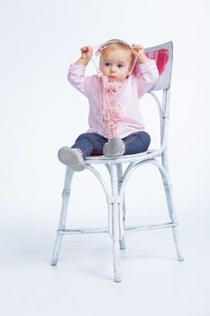 Portrait of an adorable baby girl wearing a pink with pearl necklace sitting on a c