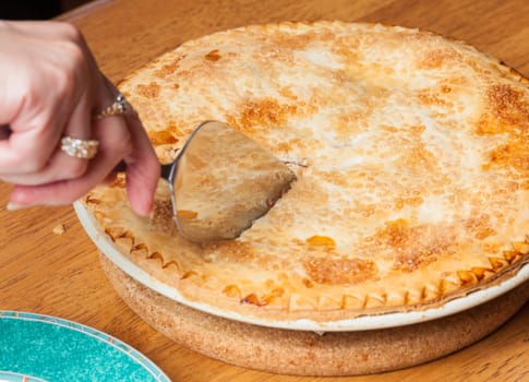 Home made baked fruit pie from oven and on table being cut with knife