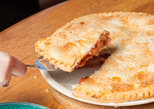 Home made baked fruit pie from oven and on table being cut with knife
