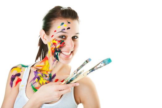A young, smiling artist with brushes and acrylic paint on her face and body.  Shot on white background.