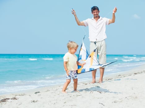 Little cute boy playing his father with a colorful kite on the tropical beach.