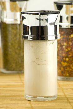 garlic powder in a glass jar on different spices background over wooden mat