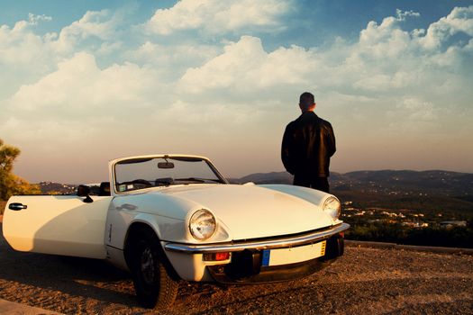 View of a young male with a jacket next to his white convertible car.