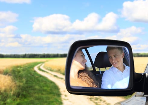 Reflection of young couple in mirror of car at countryside