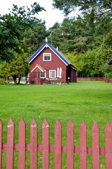 Wooden colorful house in rural homestead. Well. Fence. Green lawn yard.