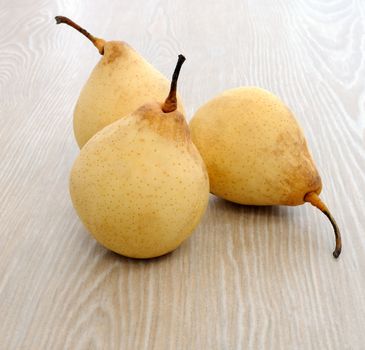 Three ripe yellow pear close to the wooden surface