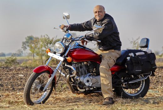 Gujarat India in a rural farmland senior male adult on his red cruiser motorcycle