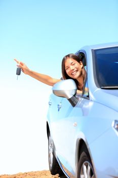 Car woman showing keys excited, happy and joyful. Young woman driver smiling in her new car. Mixed race Asian / Caucasian female model above the clouds on beautiful summer day.