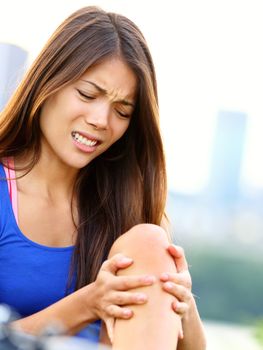 Sports injury. Woman with pain in knee joint sport workout. Young woman fitness model outside.