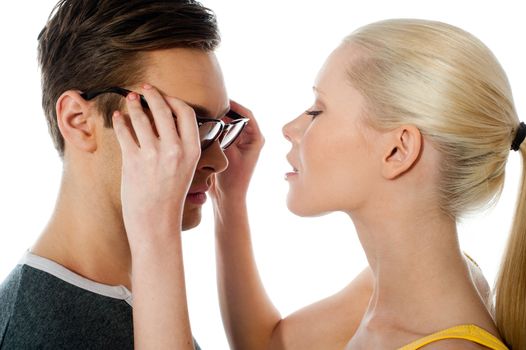Beautiful girl about to kiss her boyfriend as she removes his glasses over a white background