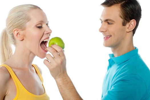 Young guy making her pretty girlfriend eat an apple. Healthy couple