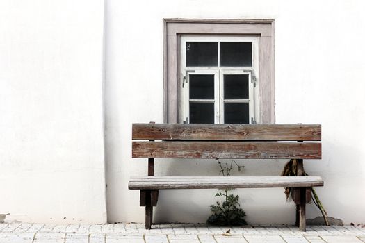 old bench in front of an weathered window with white wall