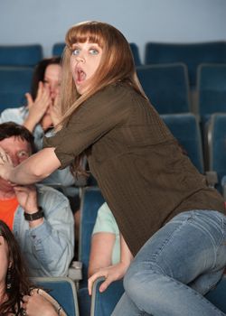Scared young Caucasian woman jumps out of her seat in theater