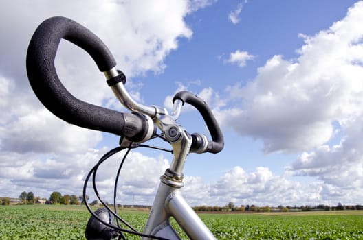 Bicycle handlebar closeup on background of blue cloudy sky. Vehicle does not require fuel. Active healthy people transportation.