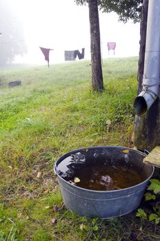 Rural life. Morning fog, laundry hanging on rope and bowl filled with water under tin gutter.