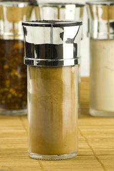 ground cinnamon powder in a glass jar on different spices background over wooden mat