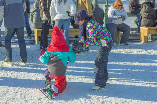 Two kids playing together in snowy cold winter day, and helping each other to learn how to ice skate in the Skating Rink in Old Port of Montreal. Quebec, Canada