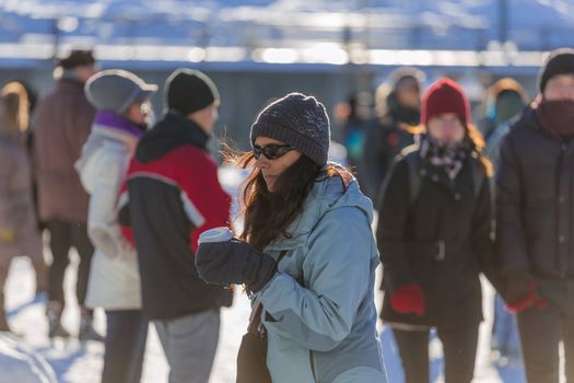 A woman ice skating with her hot coffee in a cold winter day in the Skating Rink in Old Port of Montreal, Quebec ,Canada