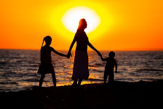 Mother and her kids silhouettes on beach at sunset